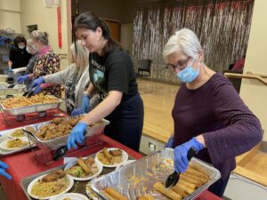 women at buffet type line serving Asian meal items